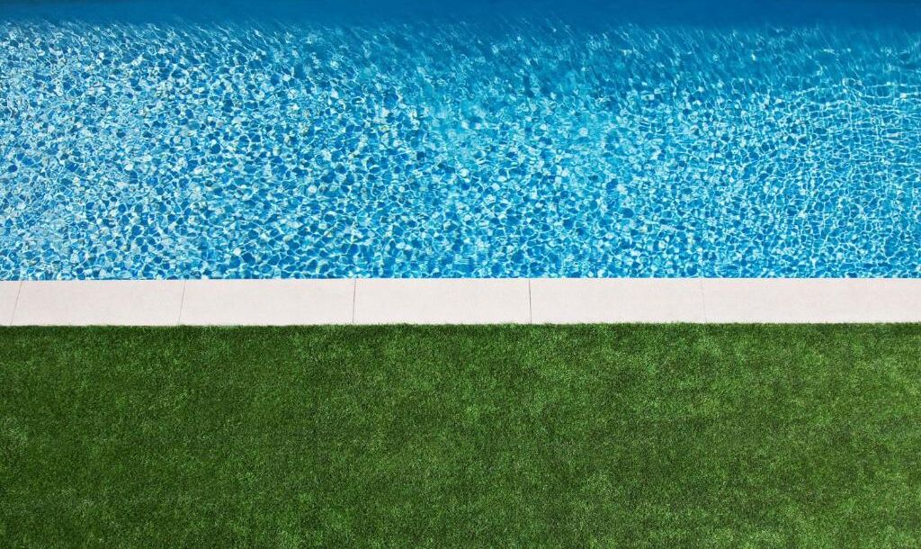 A swimming pool with clear blue water and a green artificial grass area in front.