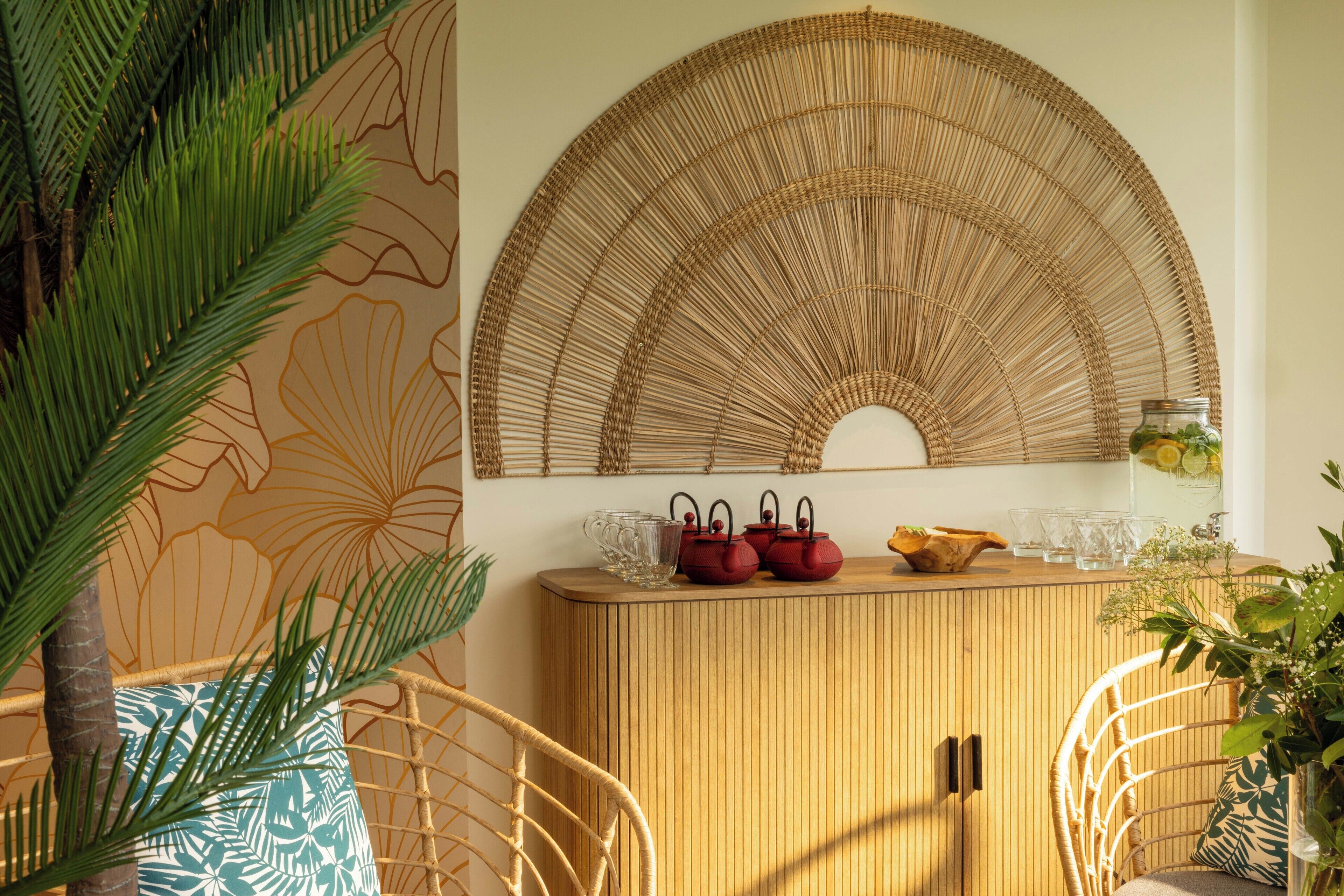 A room with a wooden cabinet, wicker chairs, and a large wall art piece.