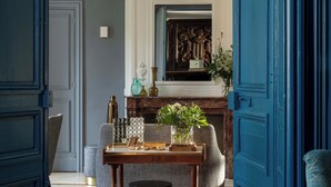 A dining area with a wooden table, two grey chairs, a small round table, and a blue door. - Hôtel Château Saint-Gilles - Bayeux (Gueron)