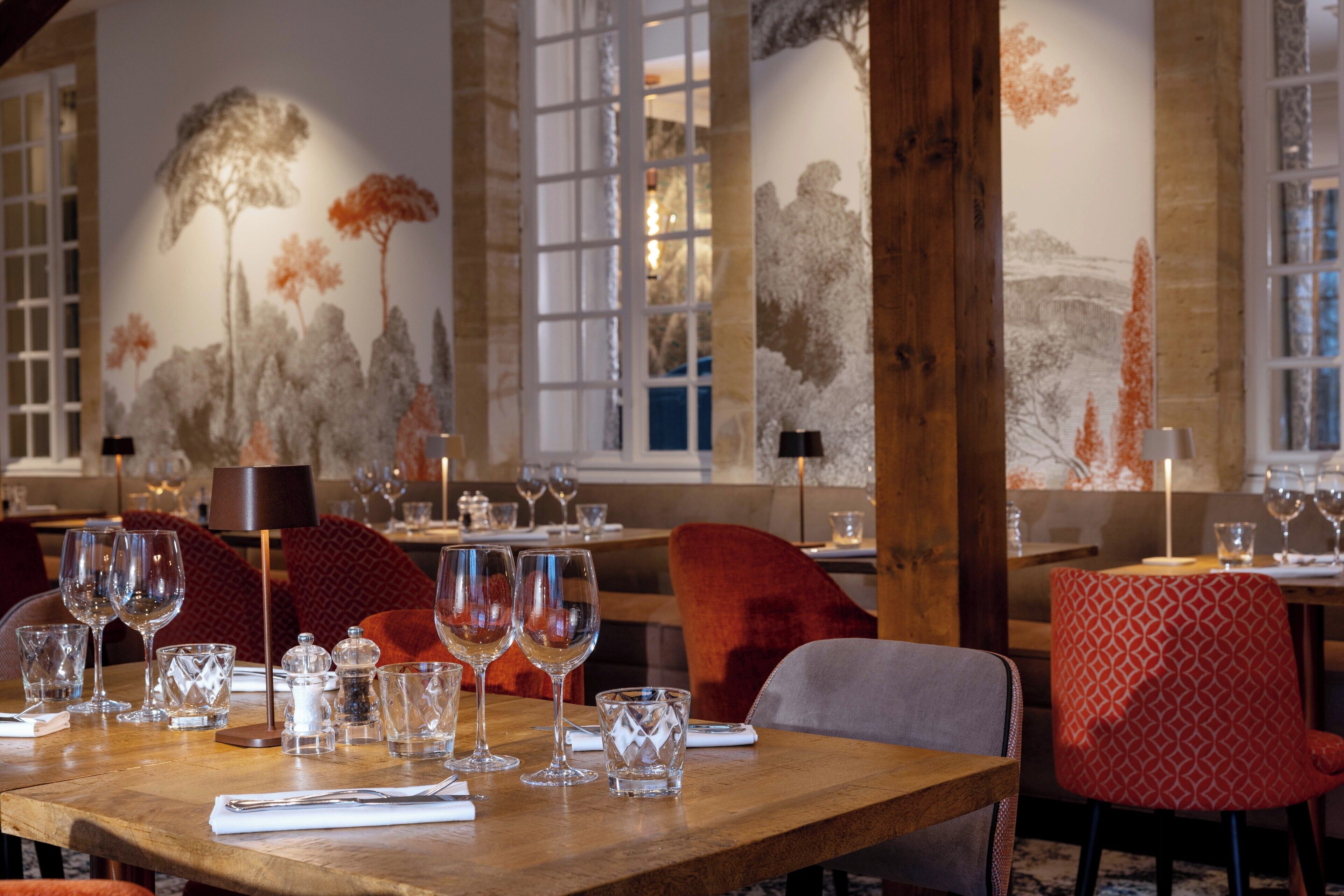 A dining area with wooden tables, red upholstered chairs, and clear glassware.