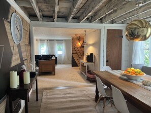 Ett rymligt vardagsrum med ett matbord i trä, en soffa och ett soffbord. Här finns också ett köksområde med en bänkskiva i trä och en hängande lampa.