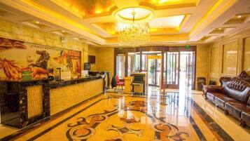 A hotel lobby with a reception desk, a chandelier, a patterned floor, and a leather sofa.