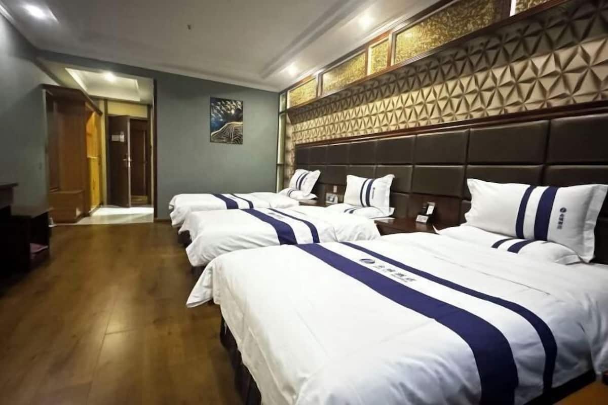 A hotel room with a large bed, a headboard with a geometric pattern, and a wooden floor.