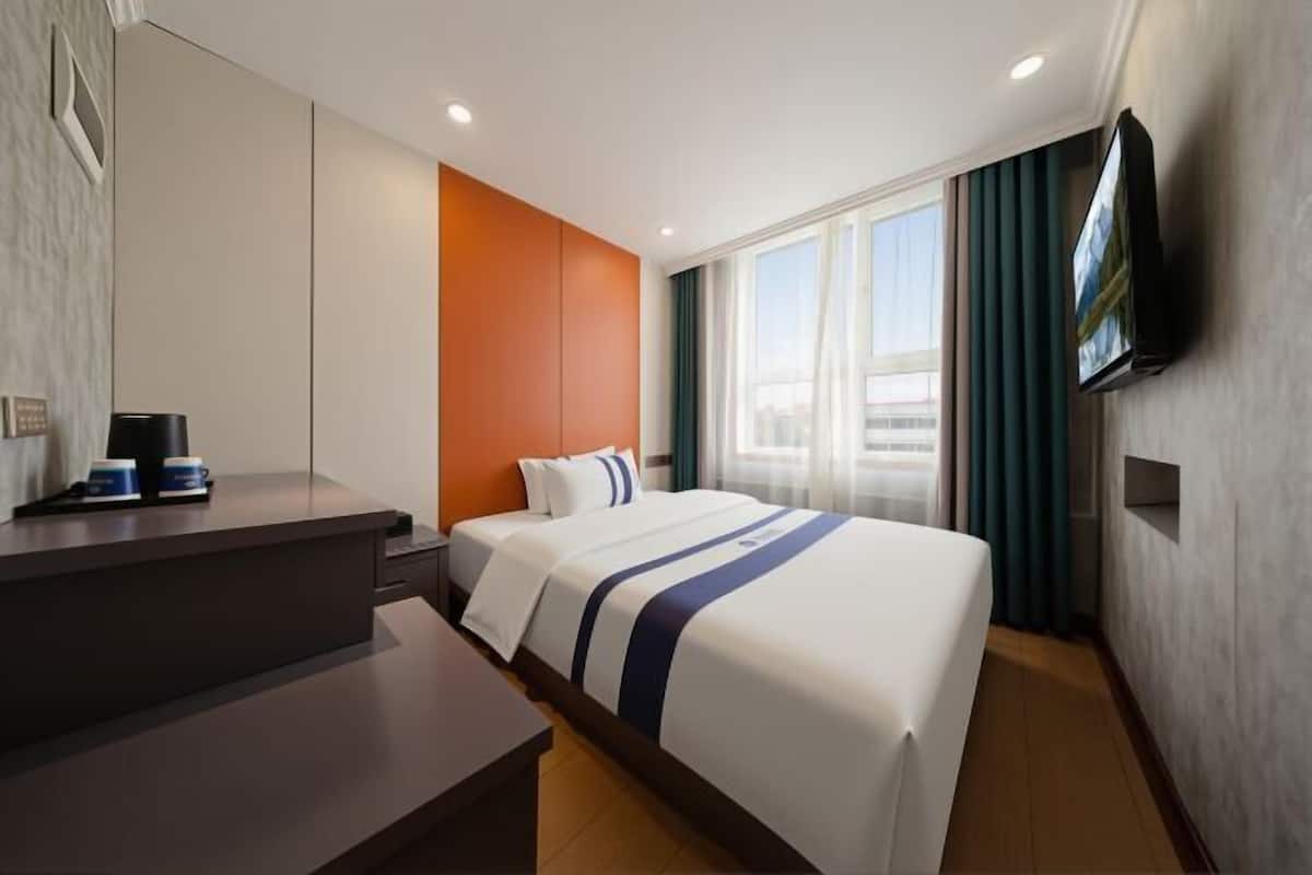 A hotel room with a bed, a desk, a TV, and a window with curtains.