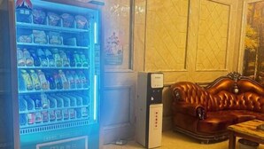 Una máquina expendedora llena de bebidas, un sofá de cuero y una mesita en una habitación con suelo de baldosas.