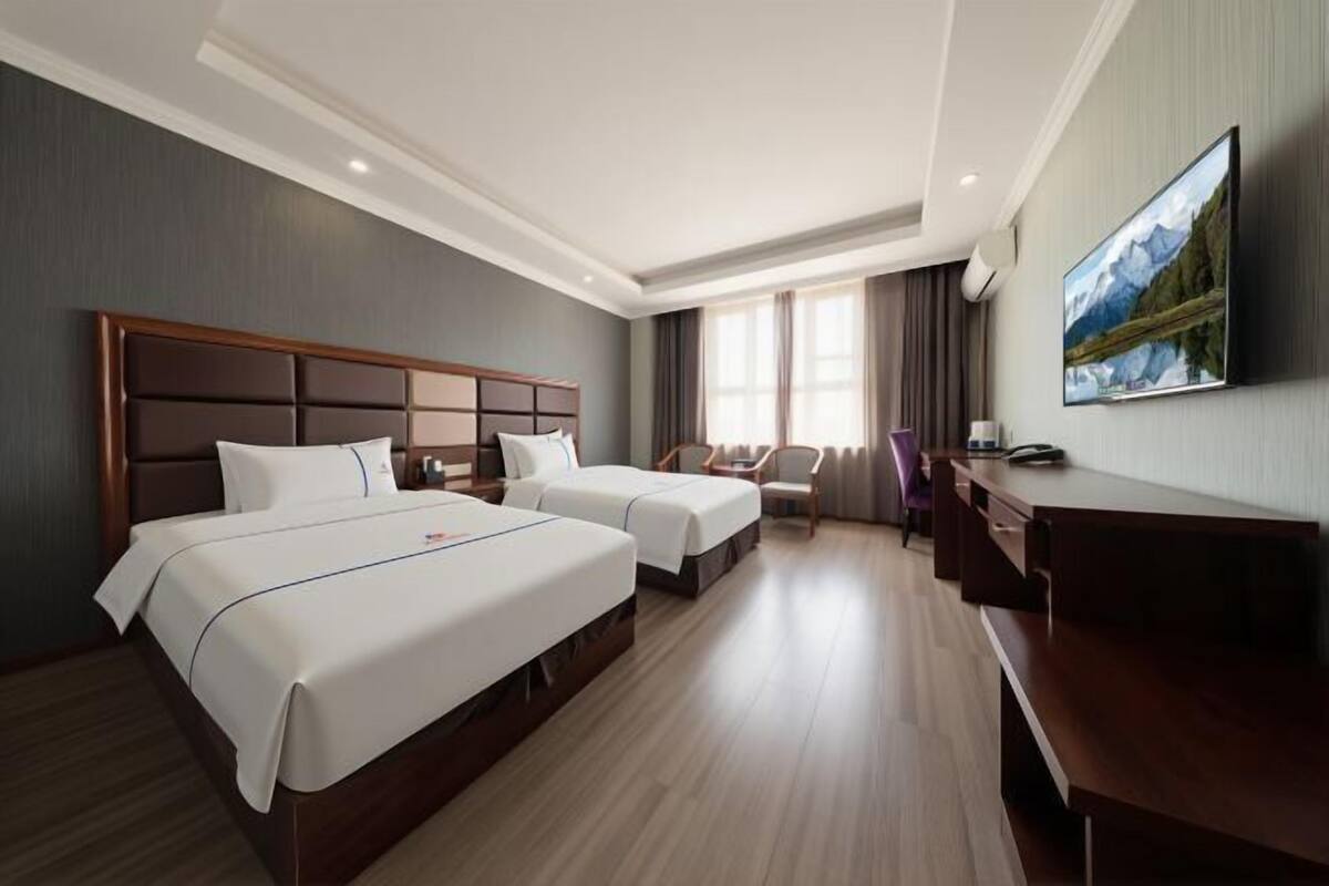 A hotel room with two beds, a desk, a chair, and a TV on the wall.