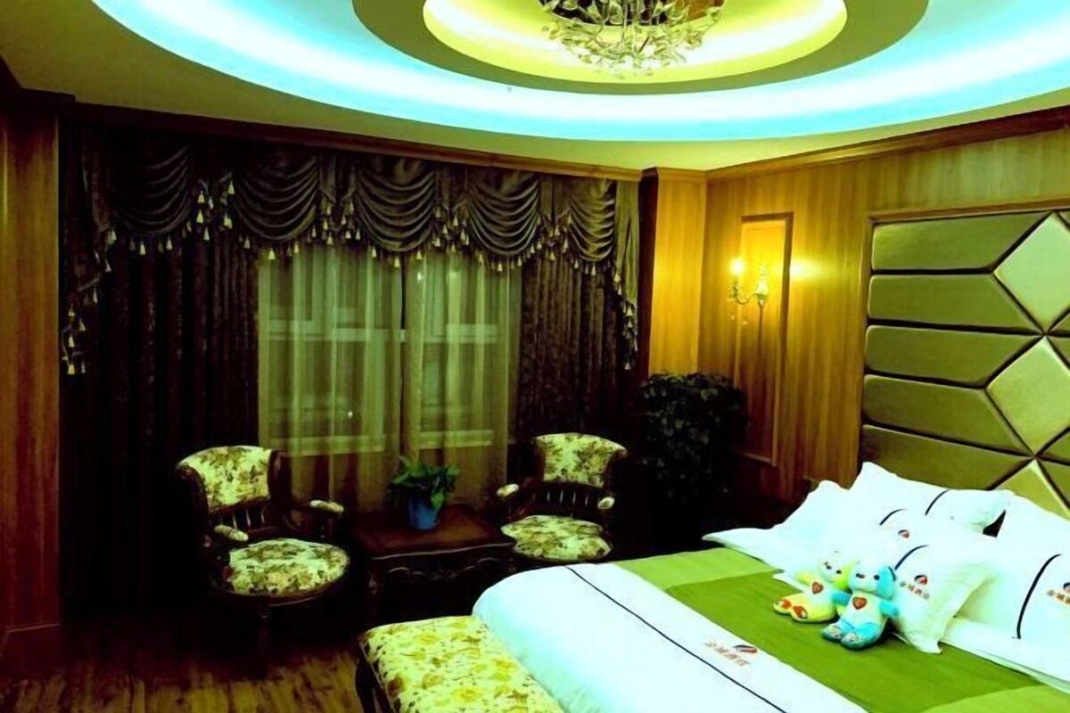 A hotel room with a bed, two armchairs, a small table with a plant, and a decorative wall panel.