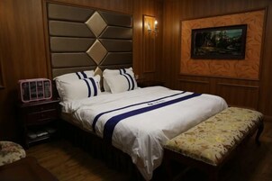 Un dormitorio con una cama, una mesita de noche, un banco, un cuadro colgado en la pared y una lámpara de pared.