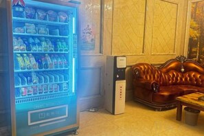 A vending machine with various beverages, a leather sofa, and a small table in a room with tiled flooring.