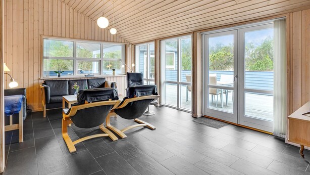 A modern interior with a wooden ceiling, large windows, and a seating area with two black chairs and a table. - Amazing home in ålbæk with sauna (Ålbæk)
