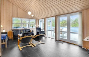 A modern interior with a wooden ceiling, large windows, and a seating area with two black chairs and a table. - Amazing home in ålbæk with sauna (Ålbæk)