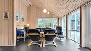 A modern interior with wooden panel walls, a large window, and a dining area with black chairs and a wooden table. - Amazing home in ålbæk with sauna (Ålbæk)