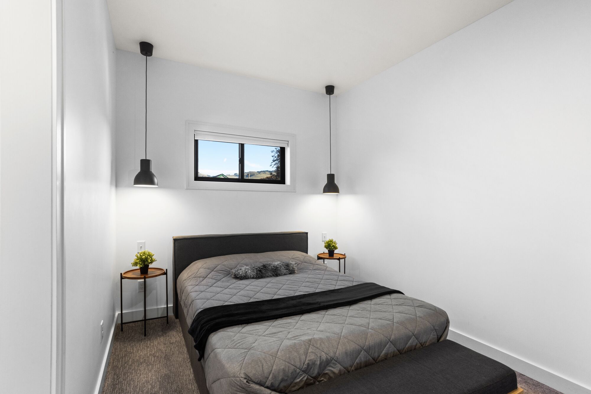 A bedroom with a bed, bedside tables, a window, and pendant lights.