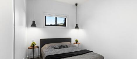 A bedroom with a bed, bedside tables, a window, and pendant lights.