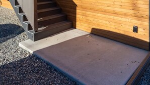A modern building with a wooden facade, a metal staircase, and a concrete ground area. - Bison Meadow Lodge #5 (Gardiner)