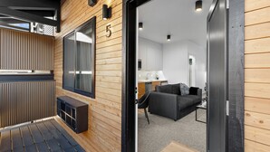 A modern interior with a wooden exterior, a number '5' on the wall, a sofa, and a kitchen area. - Bison Meadow Lodge #5 (Gardiner)
