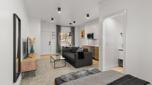 A modern living room with a sofa, a coffee table, and a TV on a wooden stand. There is a kitchen area with cabinets and a microwave. - Bison Meadow Lodge #5 (Gardiner)