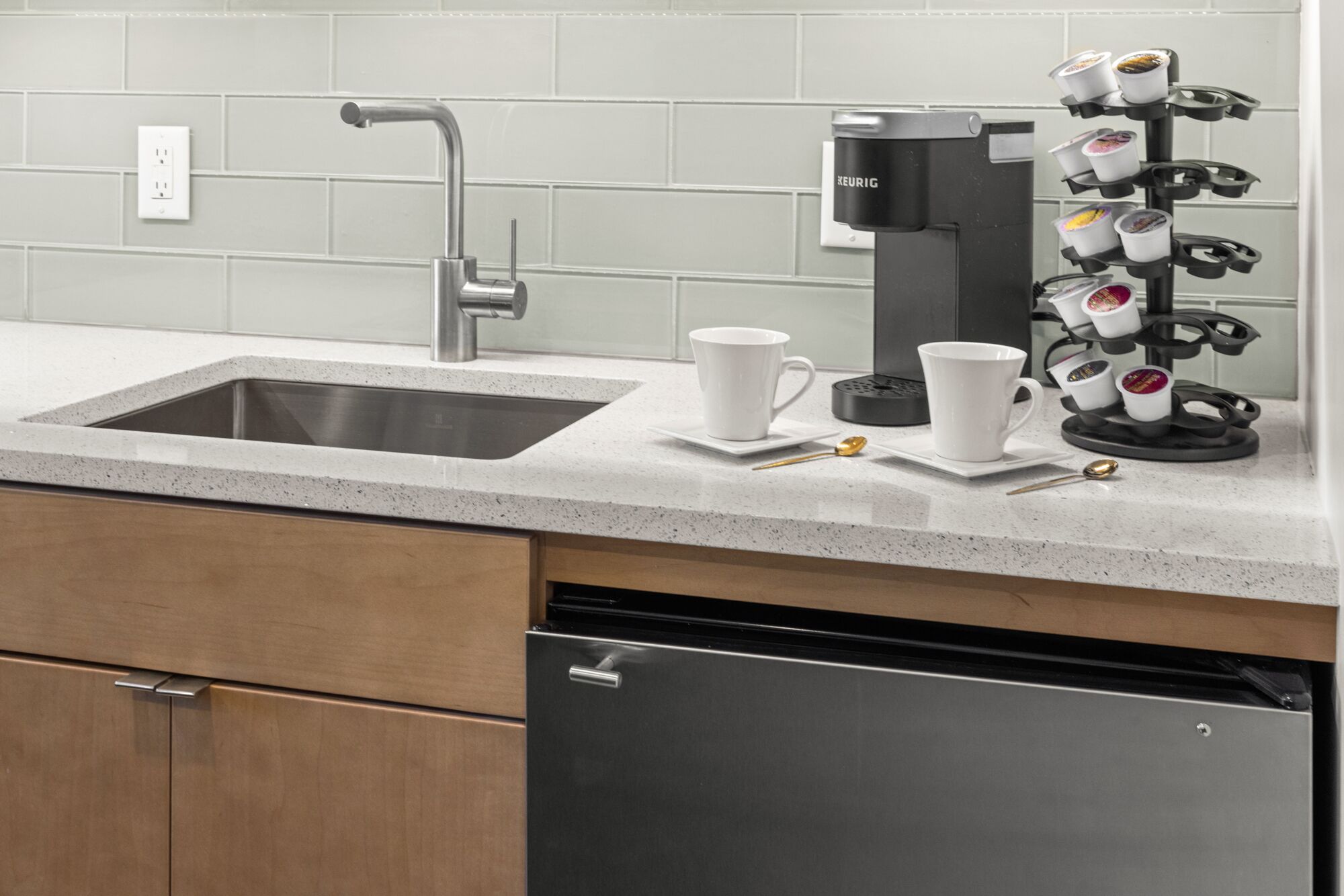 A kitchen with a stainless steel sink, a coffee maker, and a mug holder with multiple cups.