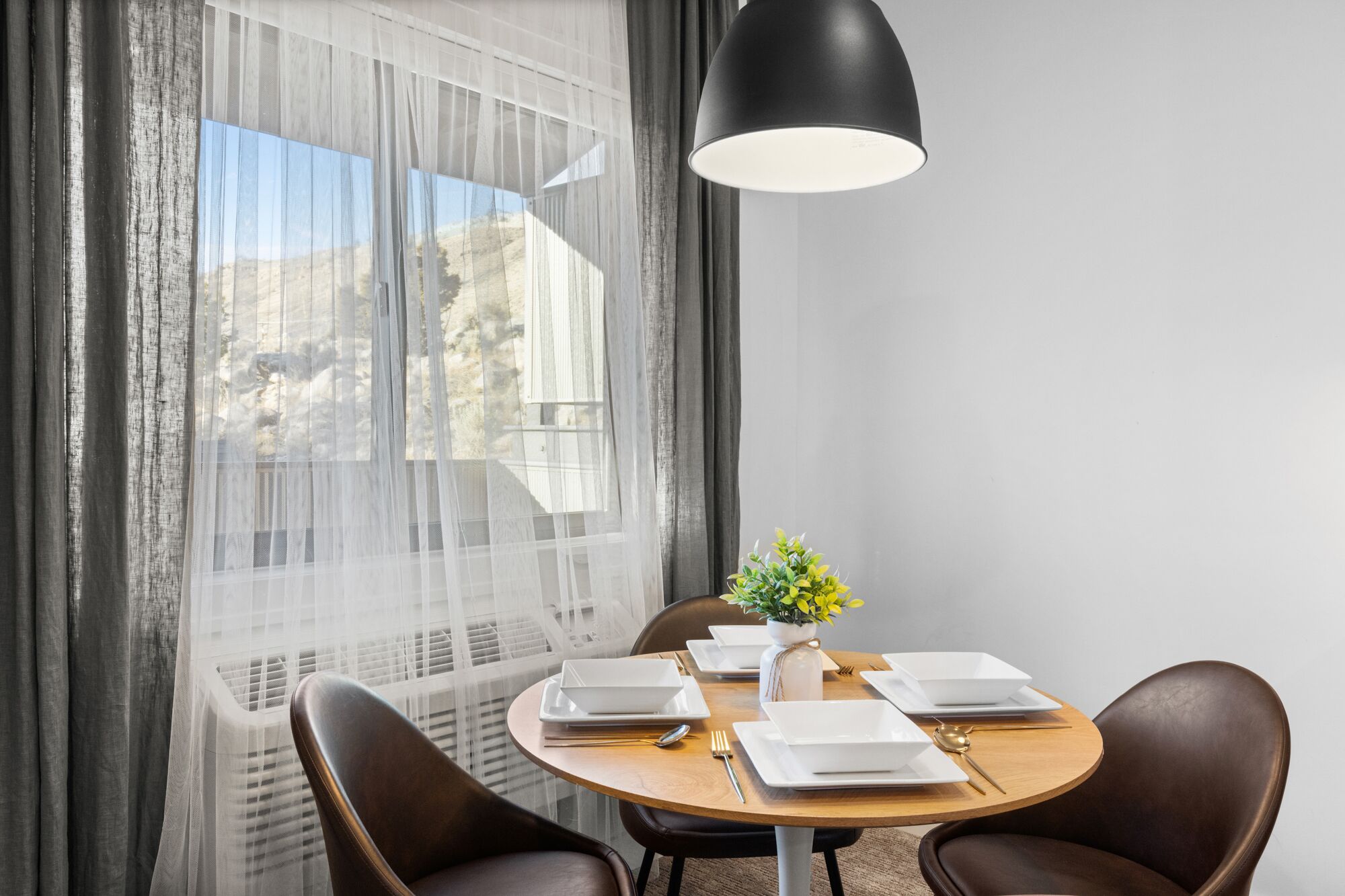 A dining area with a round table set for four, a vase with a plant, and a black pendant light.