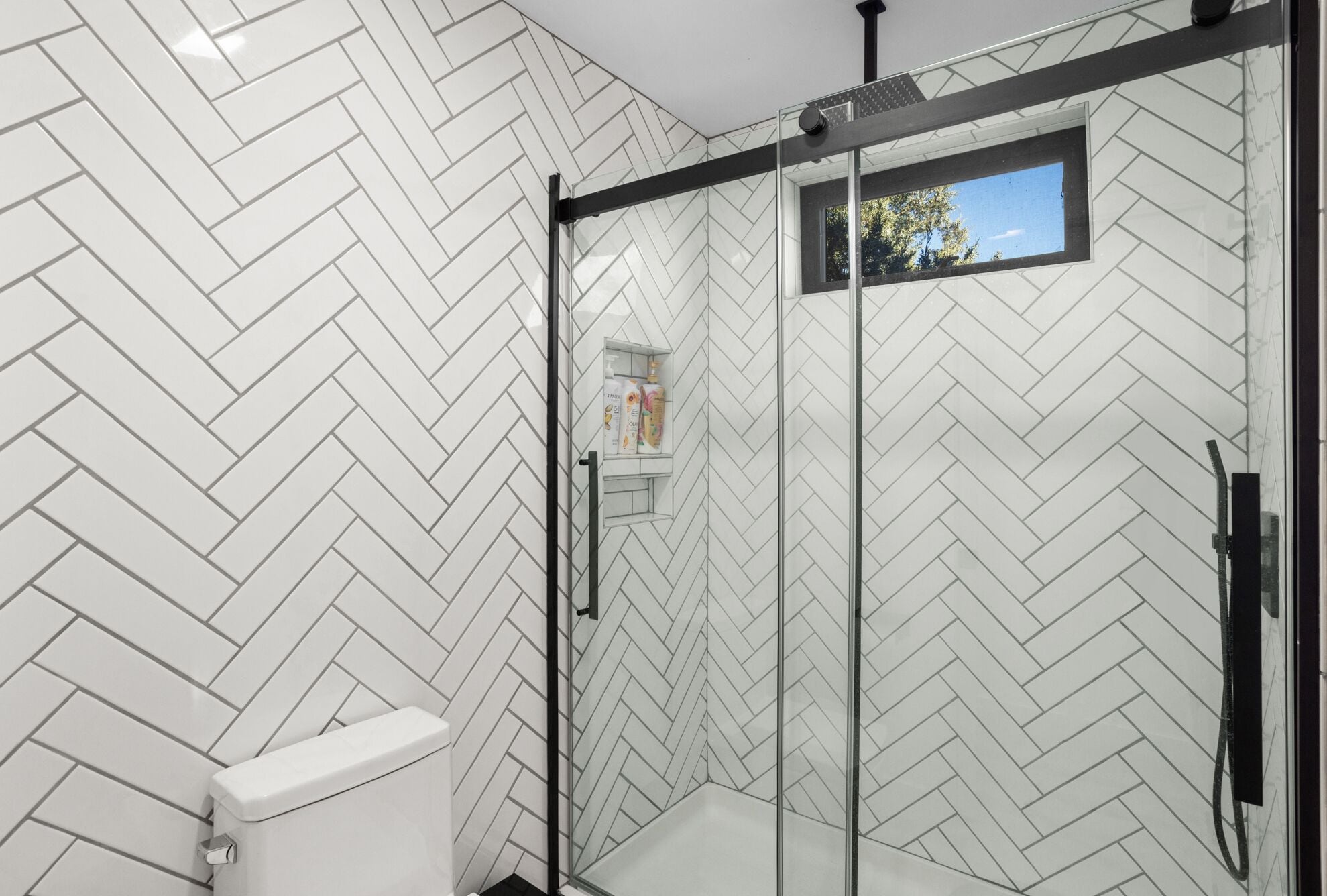 Une salle de bain moderne avec un carrelage disposé en motif de chevron, une douche en verre et une petite fenêtre.