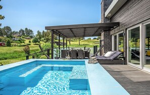 Ein Schwimmbecken mit Holzterrasse, Gartenmöbeln und Blick auf eine Wohngegend.