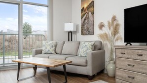 A living room with a sofa, a coffee table, a TV, a lamp, and a large window with a view of the outdoors.
