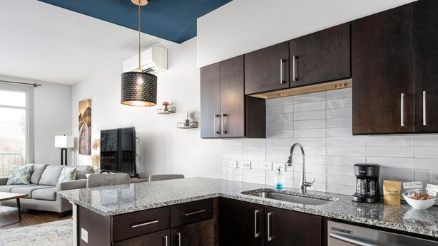 A modern kitchen with dark cabinets, a granite countertop, and a built-in dishwasher.