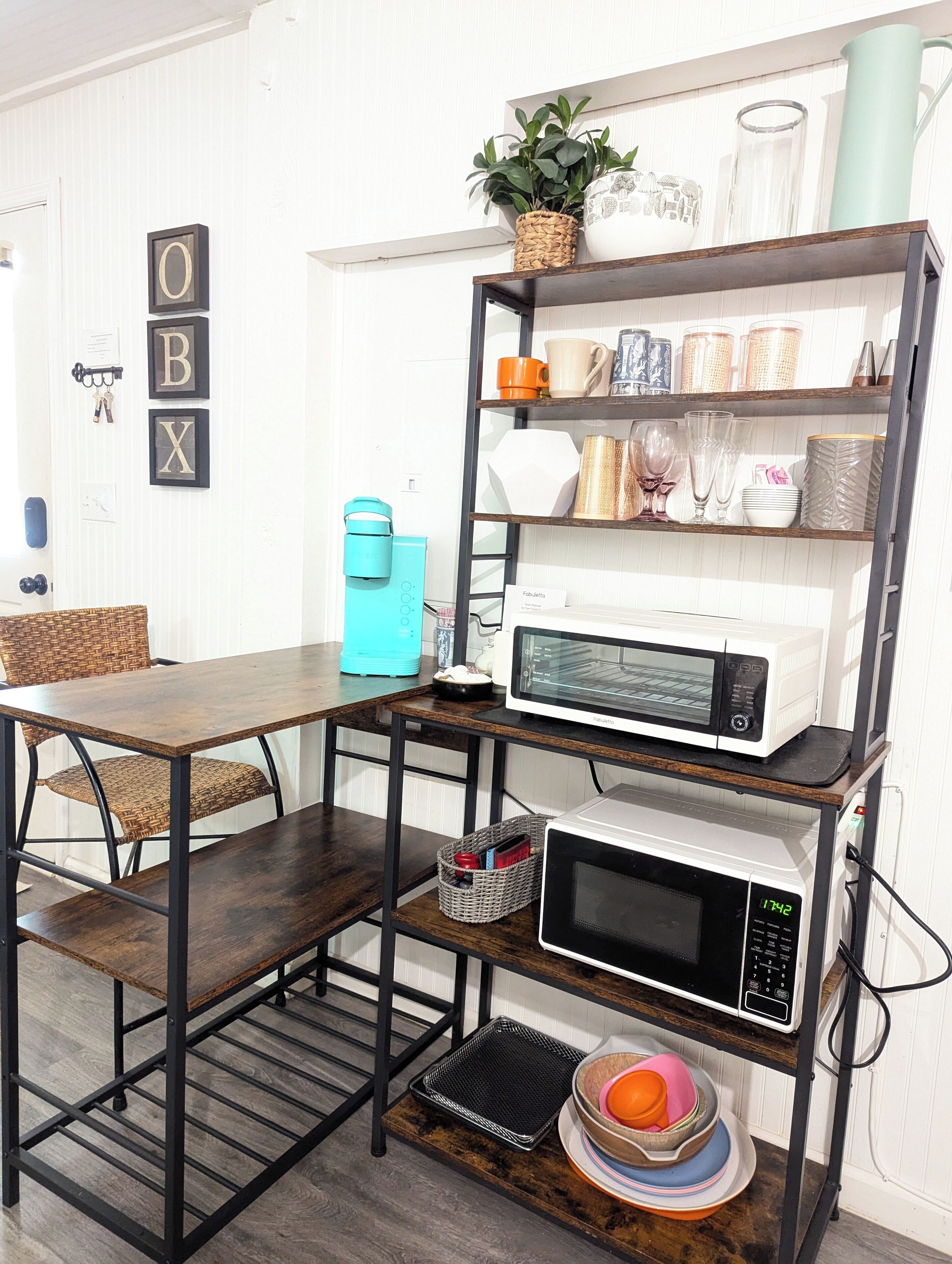 A kitchen with a wooden table, chairs, a coffee maker, a microwave, and a shelf with kitchenware.