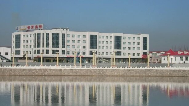 A multi-story building with a white facade and large windows, situated beside a calm body of water.