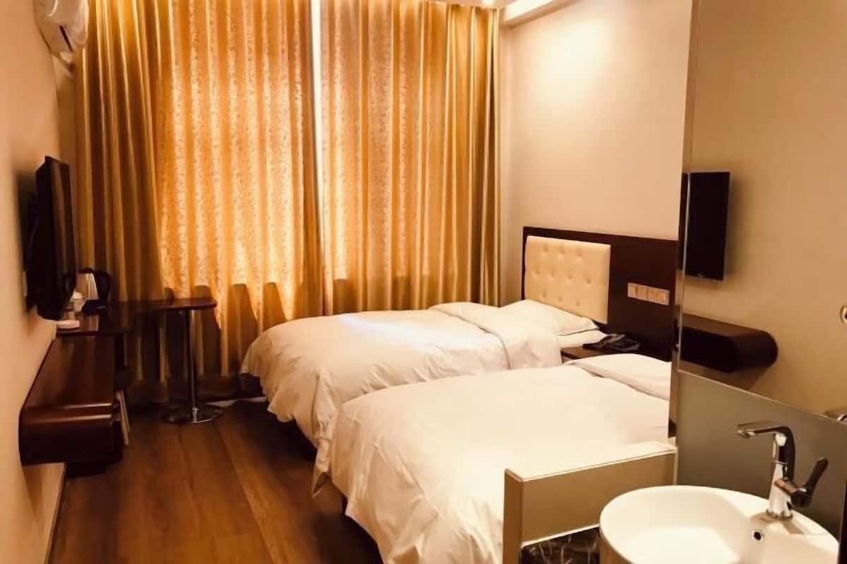 A hotel room with two beds, a small table, a mirror, and a sink.