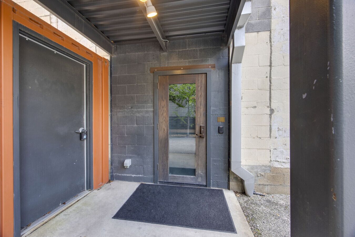 A modern entrance with a glass door, a black mat, and a metal roof.