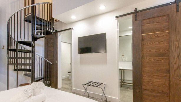 A bedroom with a bed, a TV mounted on the wall, a wooden door, and a spiral staircase. - Center Gulch - Walk to Downtown - Private Parking (Nashville)