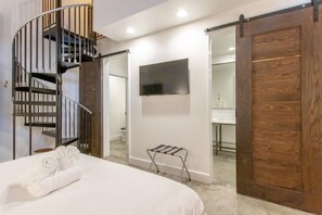 Une chambre à coucher avec un lit, un téléviseur fixé au mur, une porte en bois et un escalier en colimaçon.