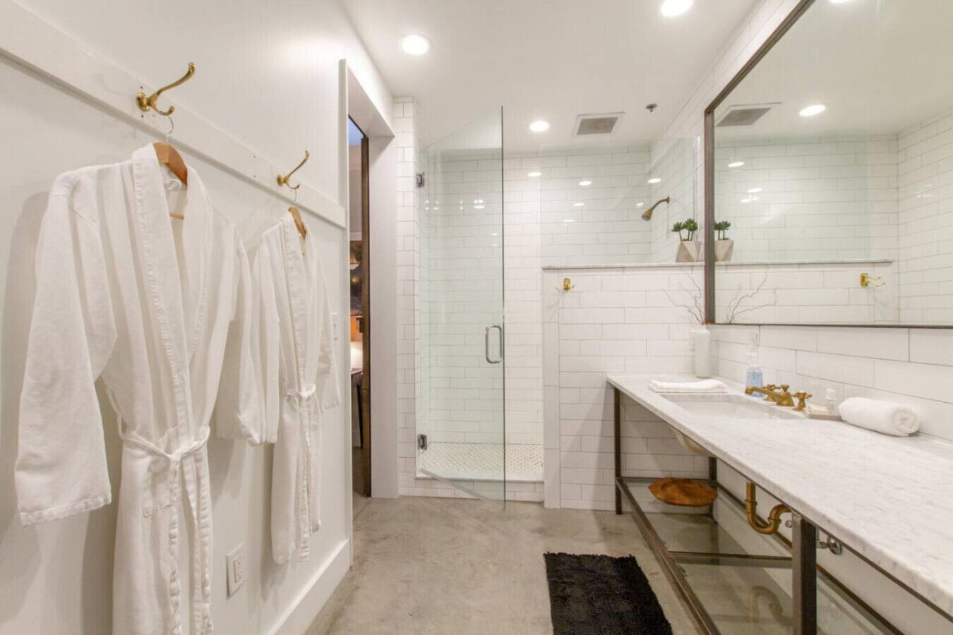 Un baño moderno con cabina de ducha de vidrio, paredes con azulejos blancos y un espejo grande sobre el lavamanos.