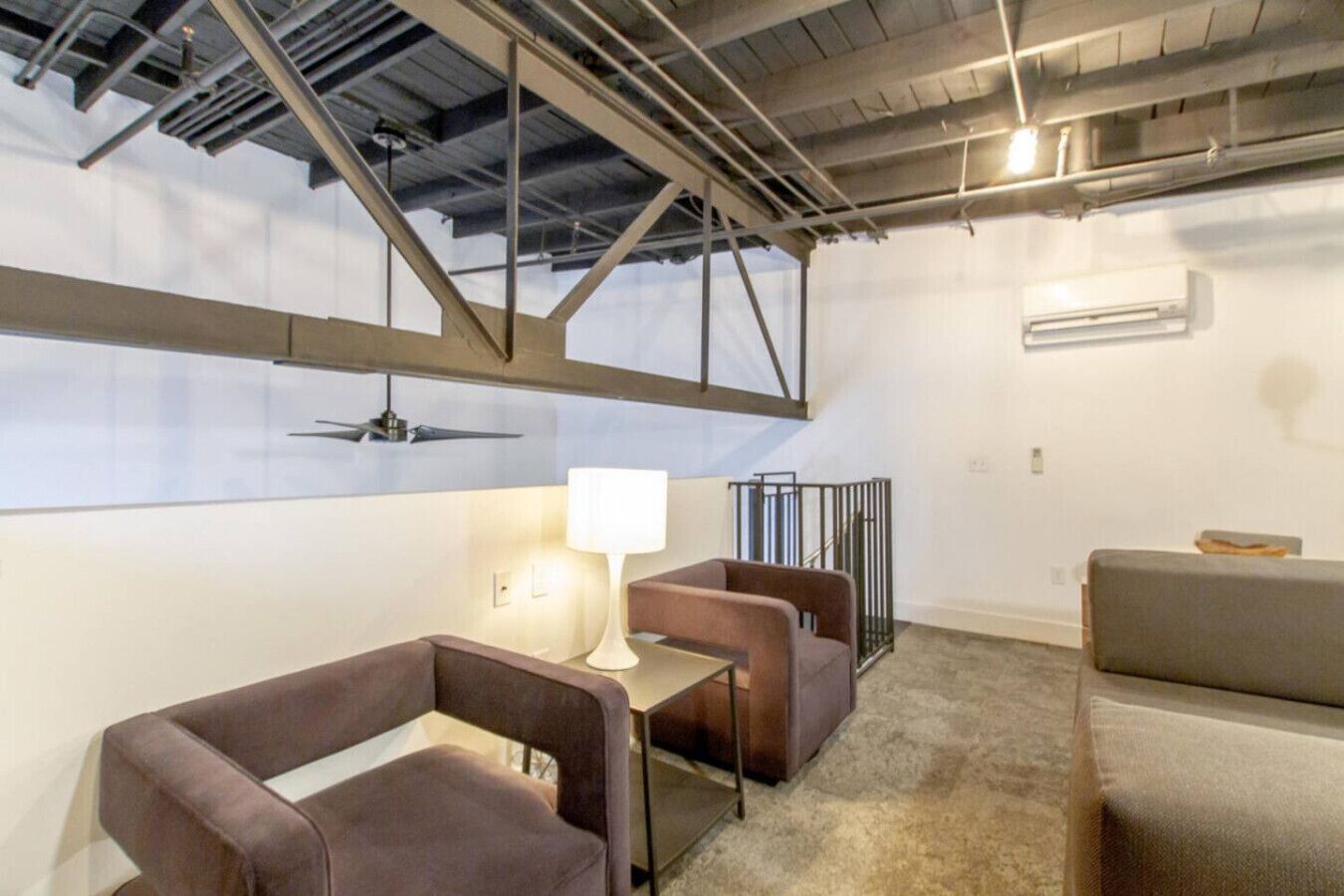 Una habitación moderna de estilo industrial con techos a la vista, ventilador de techo y una zona de estar con una mesa y sillas.