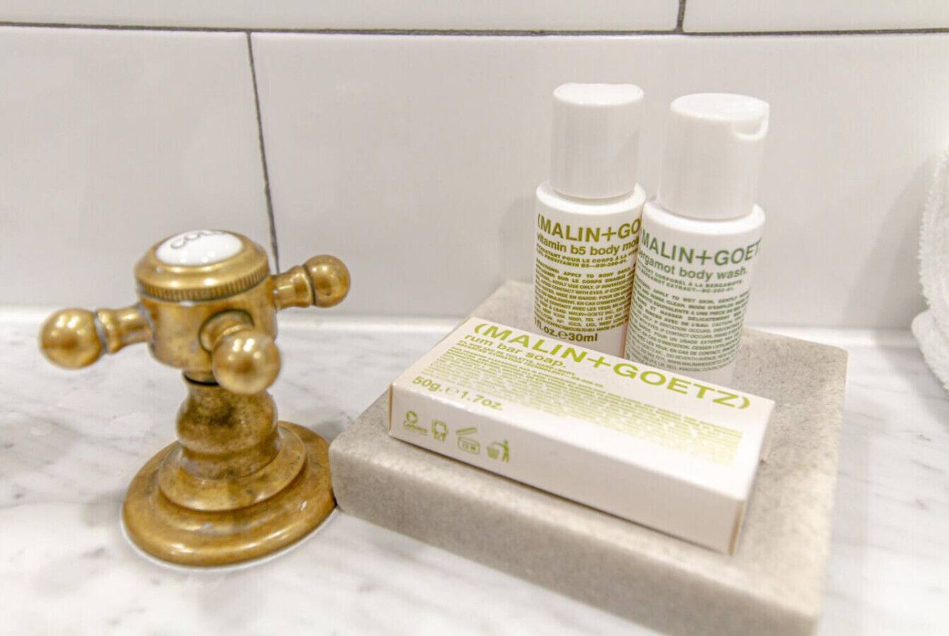 A bathroom with a marble countertop, a brass faucet, and two bottles of MALIN+GOETZ body wash.
