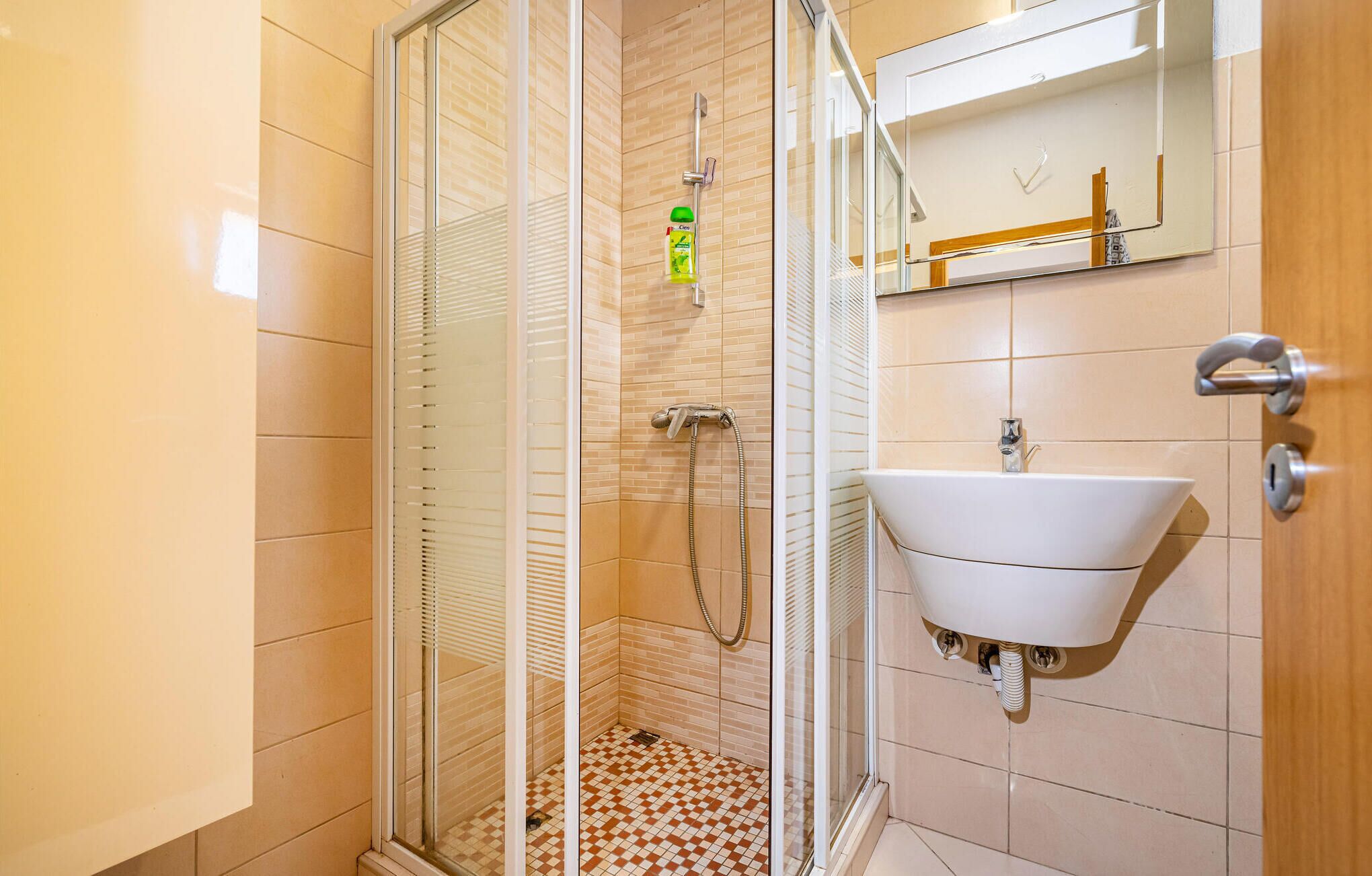 Un bany amb una cabina de dutxa de vidre, un lavabo blanc i un mirall sobre el lavabo.