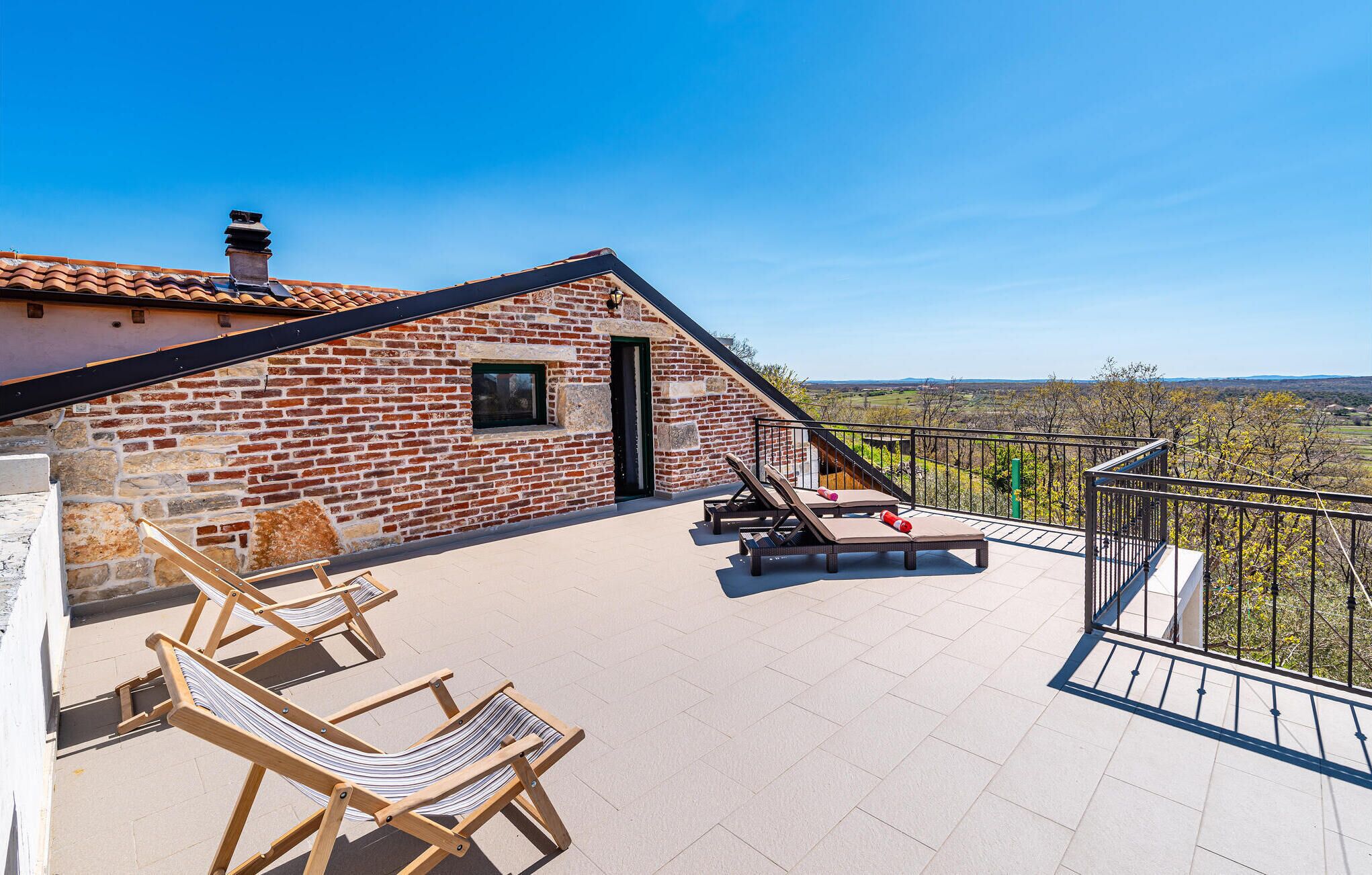 A brick building with a balcony, two lounge chairs, and a table.