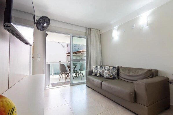Un salon moderne avec un canapé, un ventilateur et une porte-fenêtre coulissante donnant sur un balcon.