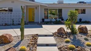 A modern house with a yellow door, a cactus garden, and a paved driveway. - Located in the famous Movie Colony neighborhood close to Downtown. (Palm Springs)