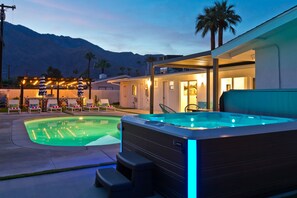 Ein Whirlpool mit blauen LED-Leuchten, ein Pool, Liegestühle und eine Bergkulisse.
