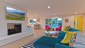 A modern living room with a fireplace, a teal sofa, and a large TV mounted on the wall. - Located in the famous Movie Colony neighborhood close to Downtown. (Palm Springs)