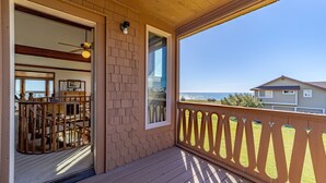 A wooden deck with a railing, a door leading to an interior space, and a view of the ocean.