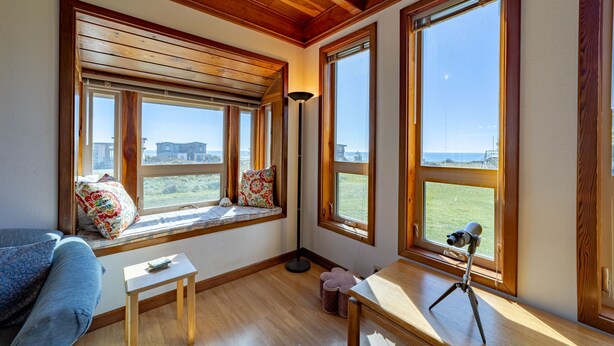 A room with large windows, a wooden ceiling, a sofa, a small table, and a telescope on a tripod.