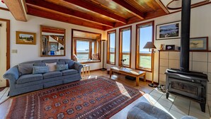 A cozy living room with a wooden ceiling, a large window, a sofa, a rug, and a fireplace.