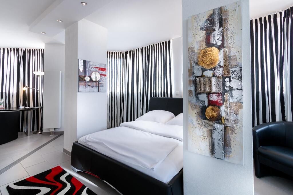 Un dormitorio moderno con una cama, un sillón de cuero negro y una obra de arte original en la pared.