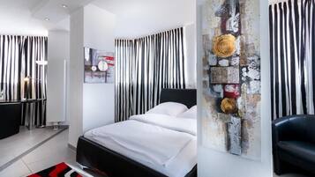 Un dormitorio moderno con una cama, un sillón de cuero negro y una obra de arte original en la pared.