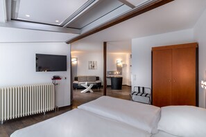 A modern hotel room with a large bed, a TV mounted on the wall, a radiator, a wooden door, and a small seating area with a sofa and table. - Turmhotel Rhein Main (Dreieich)