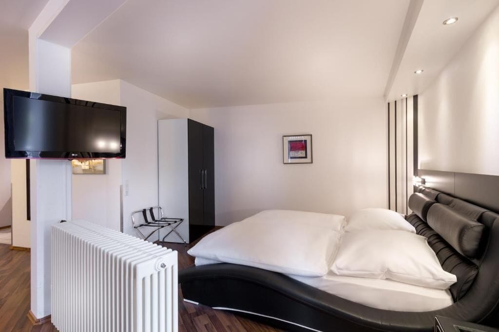A modern hotel room with a bed, a flat-screen TV, a radiator, and a framed picture on the wall.