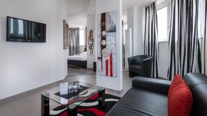 A modern living room with a black leather sofa, a glass coffee table, and a flat-screen TV mounted on the wall. - Turmhotel Rhein Main (Dreieich)